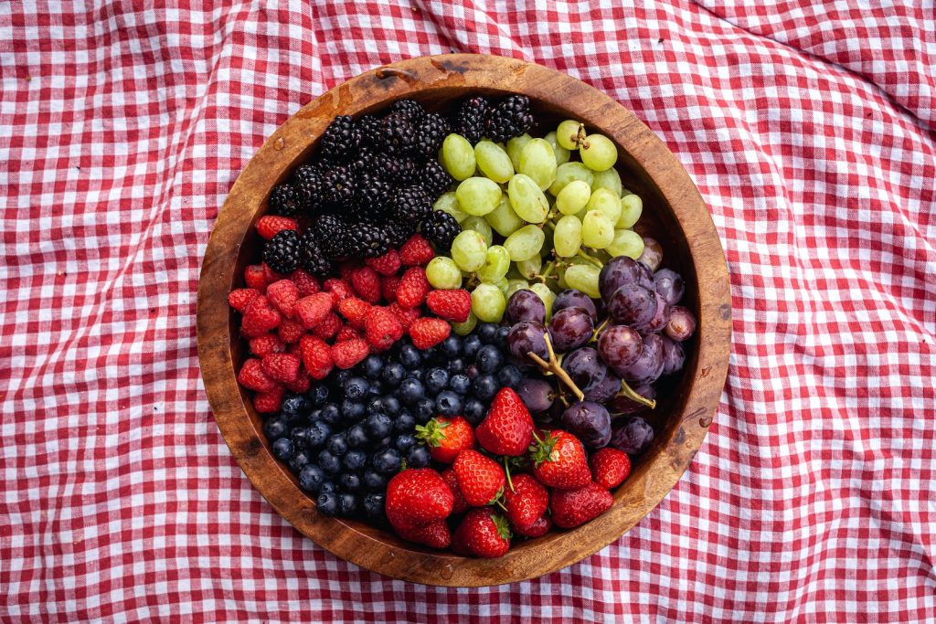 a wooden bowl filled with berries and grapes