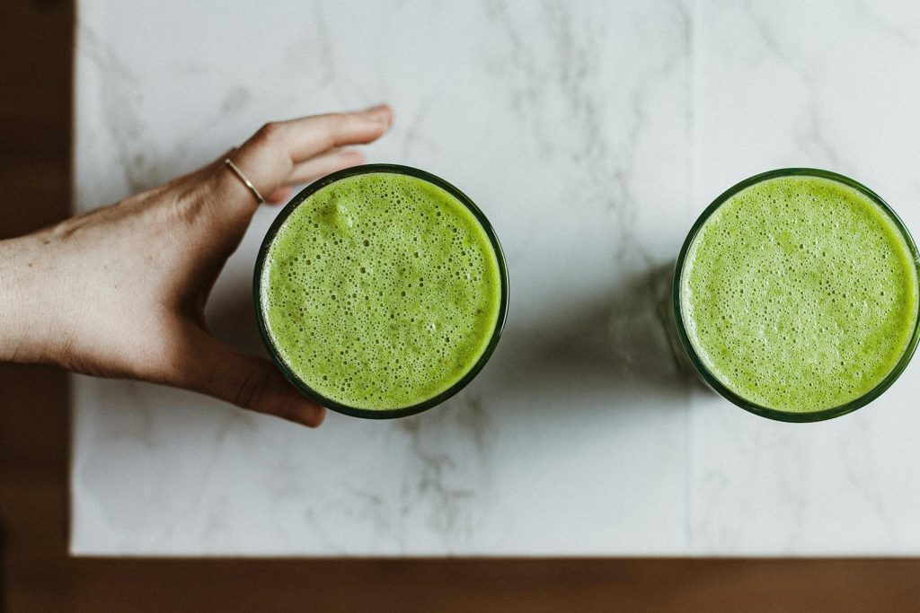 person holding green liquid in clear drinking glass